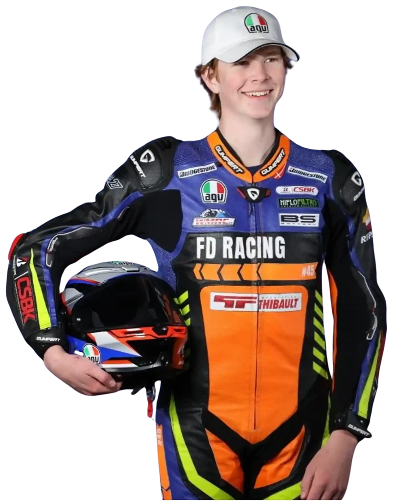 Andrew Van Winkle stanginding in his race leathers holding a helmit un his side wearing a baseball cap.